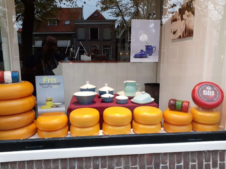Een kaasstolp in de etalage van wijn- en kaasspeciaalzaak Edam. Met blauw Jubilant, melkkan en een broodschaal.